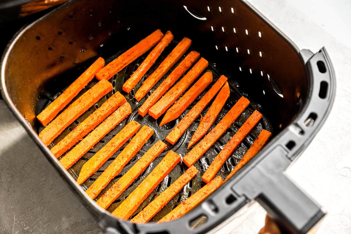 Seasoned sweet potato fries arranged in a single layer inside an air fryer basket before cooking.