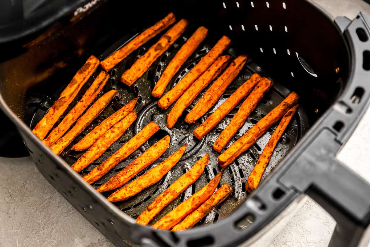 Fully cooked air fryer sweet potato fries golden and crispy inside the air fryer basket.