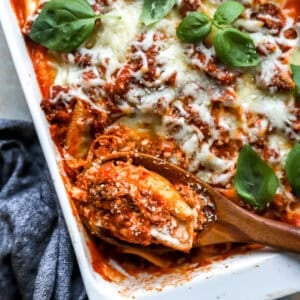 Baked Italian stuffed shells with meat sauce and melted mozzarella cheese in a white baking dish garnished with fresh basil