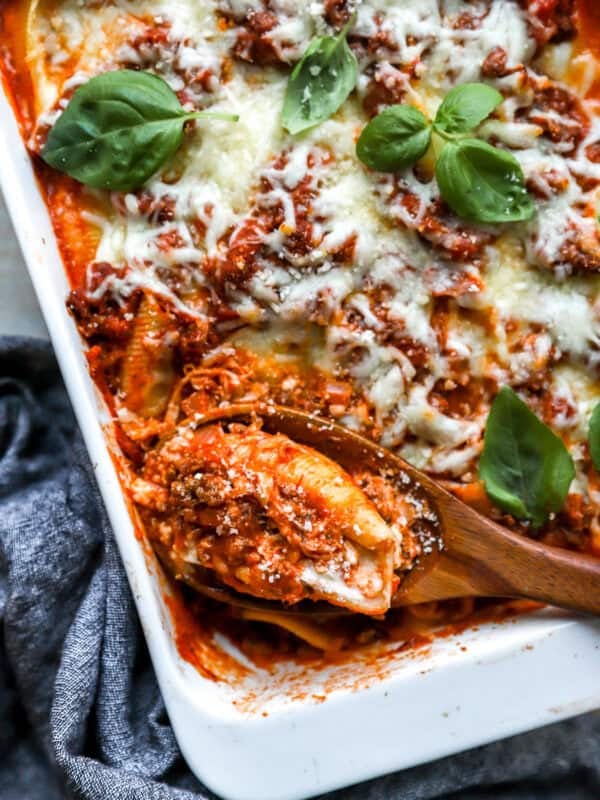 Baked Italian stuffed shells with meat sauce and melted mozzarella cheese in a white baking dish garnished with fresh basil