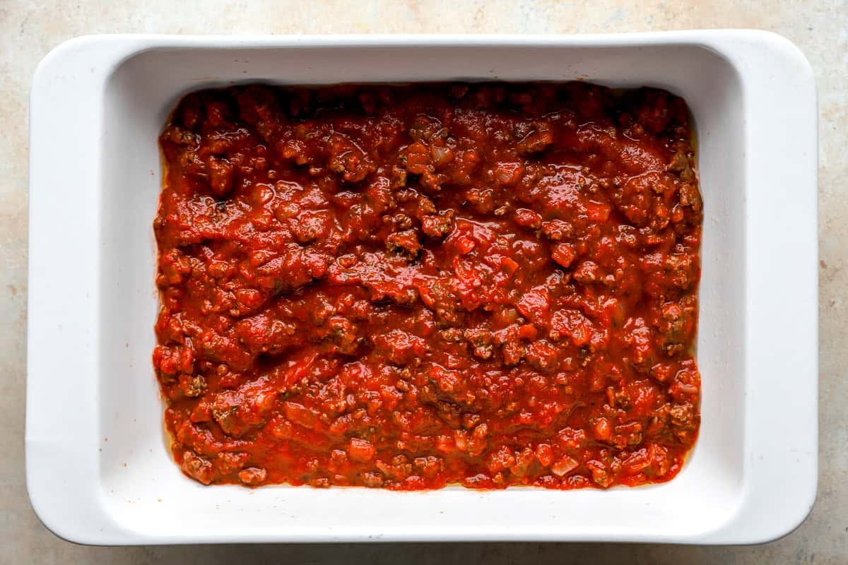 meat sauce layered in casserole dish for Italian stuffed shells