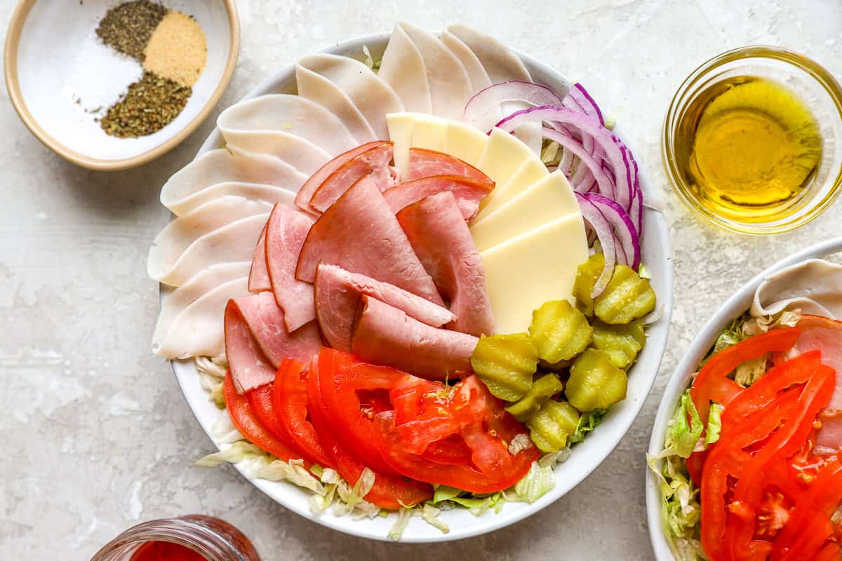 Overhead view of Italian sub salad ingredients arranged in a bowl with olive oil and seasoning nearby