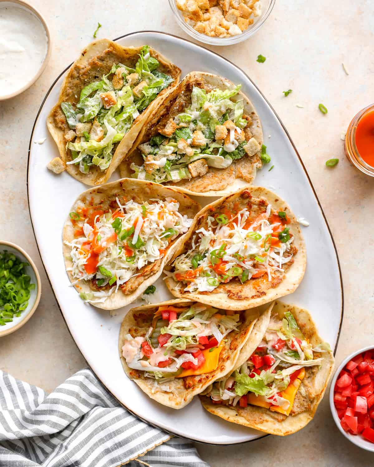 Chicken smash tacos three ways on a serving platter with Caesar, buffalo chicken, and cheeseburger toppings.