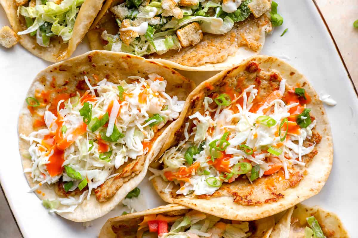 Buffalo chicken smash tacos topped with ranch slaw, green onions, and buffalo sauce on crispy flour tortillas.