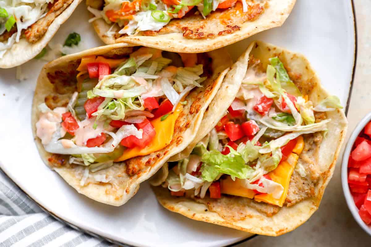 Cheeseburger chicken smash tacos topped with American cheese, lettuce, pickles, tomatoes, and burger sauce.