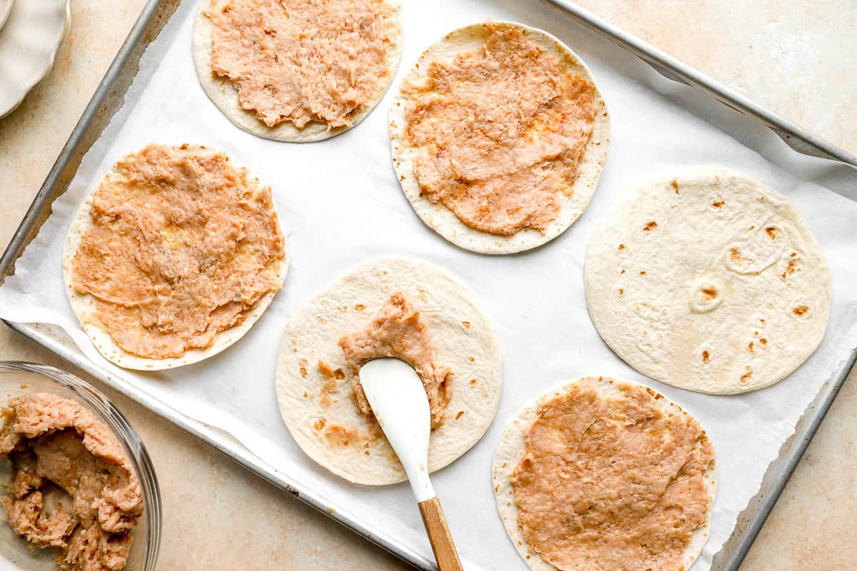 Ground chicken spread thinly onto small flour tortillas on a baking sheet for chicken smash tacos.