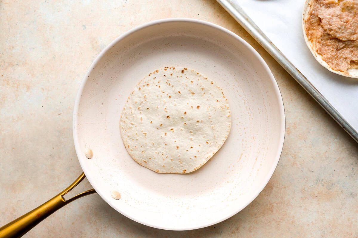 Chicken smash taco cooking meat-side down in a skillet until browned and crispy.
