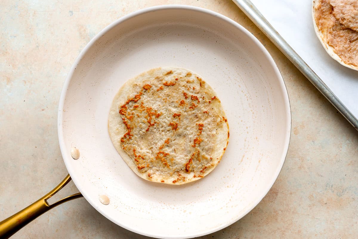 Flour tortilla placed in a skillet with cooked smashed chicken.