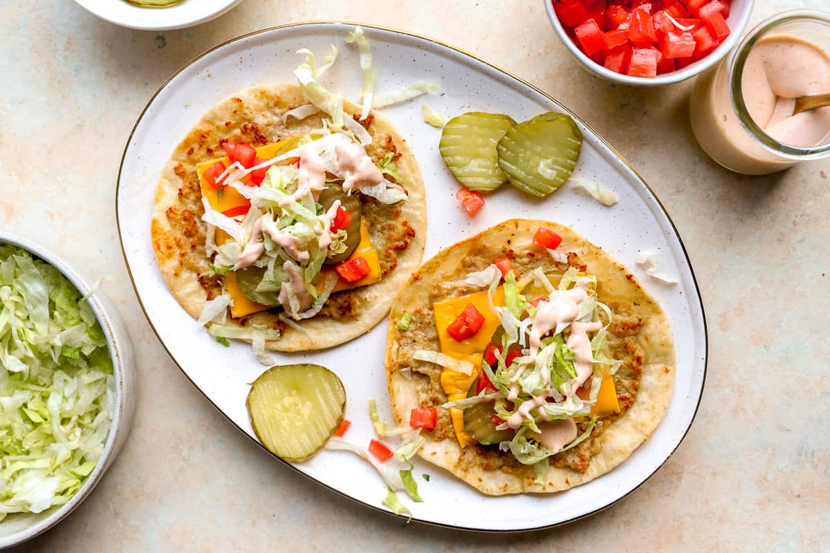 Chicken smash tacos topped with American cheese, lettuce, pickles, tomatoes, and burger sauce.