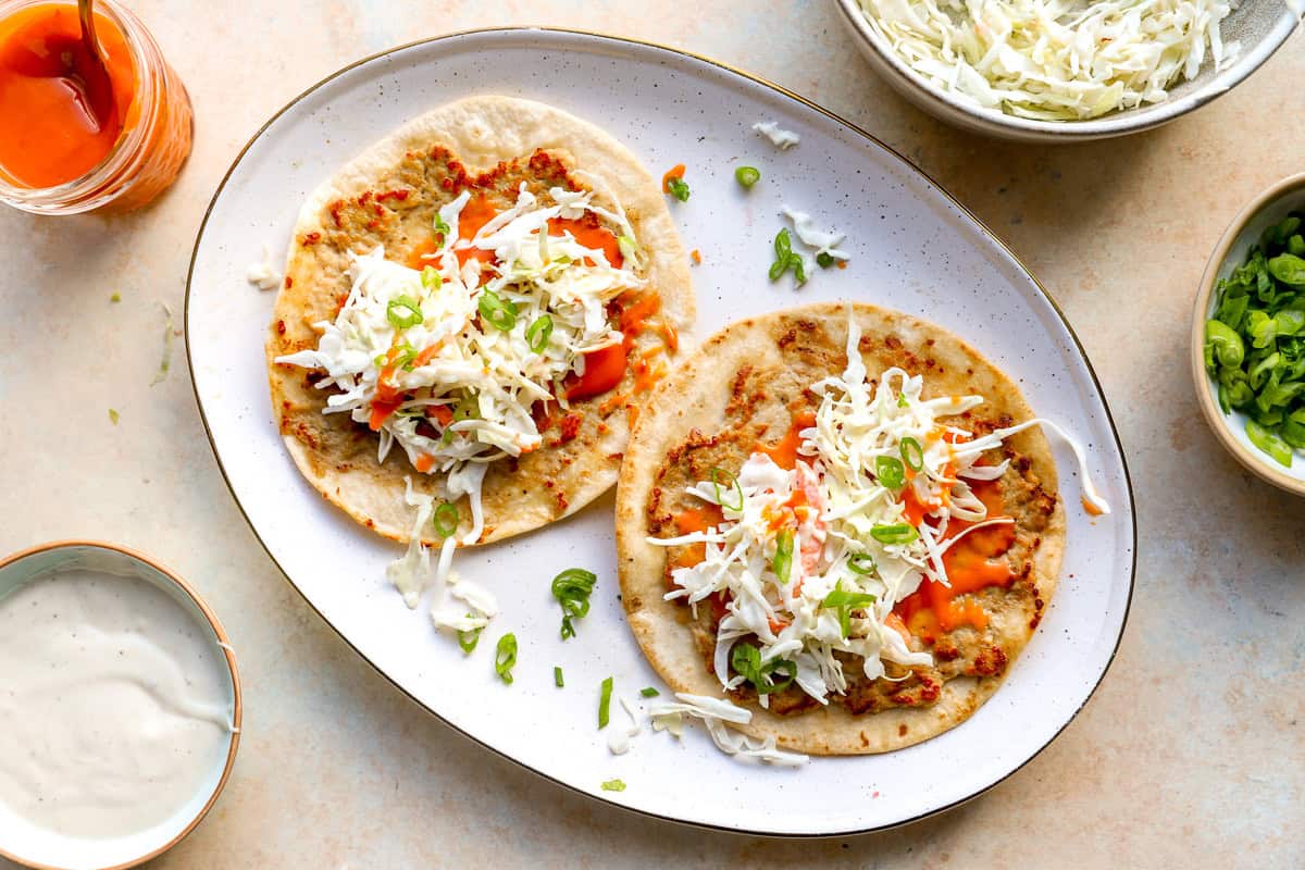 Buffalo chicken smash tacos topped with coleslaw, green onions, and buffalo sauce.