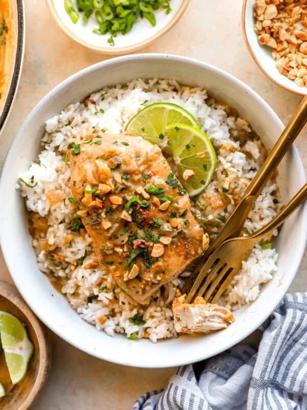 Coconut chicken served over white rice topped with chopped peanuts, cilantro, and lime slices in a bowl