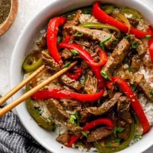 Crockpot pepper steak with tender beef strips, red and green bell peppers, and onions served over white rice with green onions.