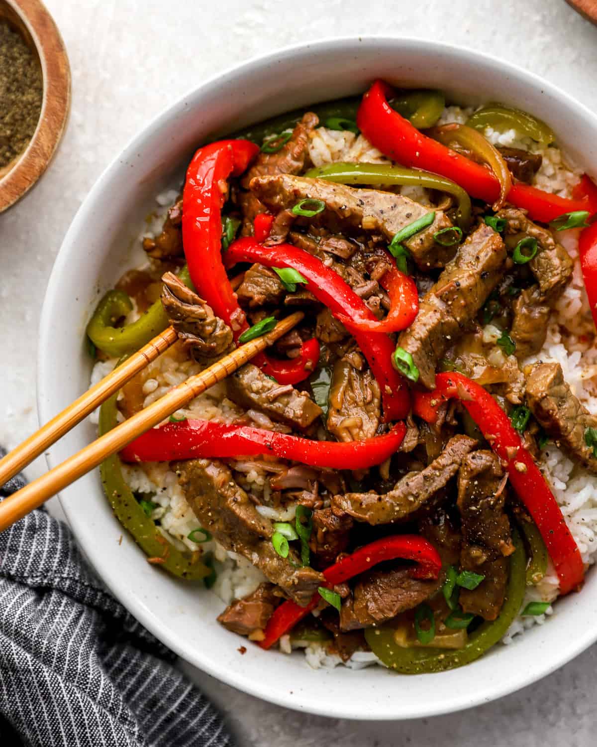 Crockpot pepper steak with tender beef strips, red and green bell peppers, and onions served over white rice with green onions.
