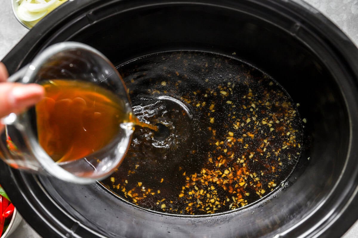 Soy sauce, garlic, ginger, and beef broth mixture being poured into a crockpot for pepper steak.