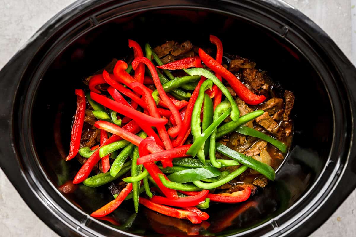 Sliced red and green bell peppers added to the crockpot pepper steak near the end of cooking.