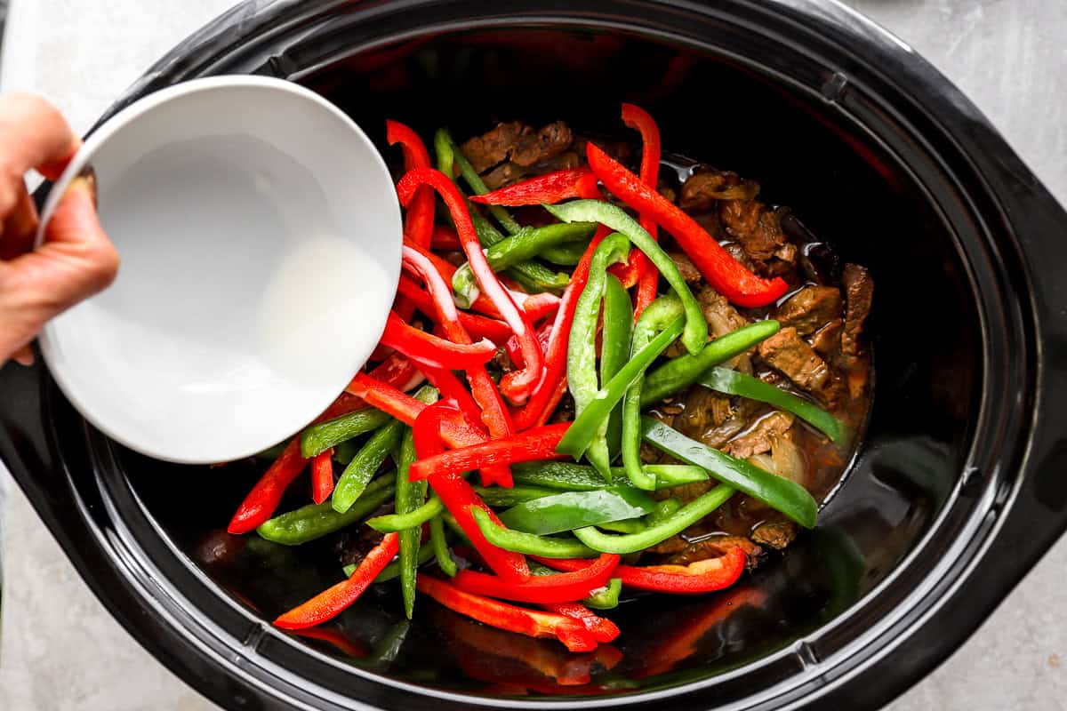 Cornstarch slurry being poured into crockpot pepper steak to thicken the sauce.