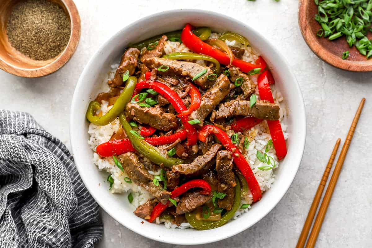 Crockpot pepper steak served over rice with bell peppers and green onions.