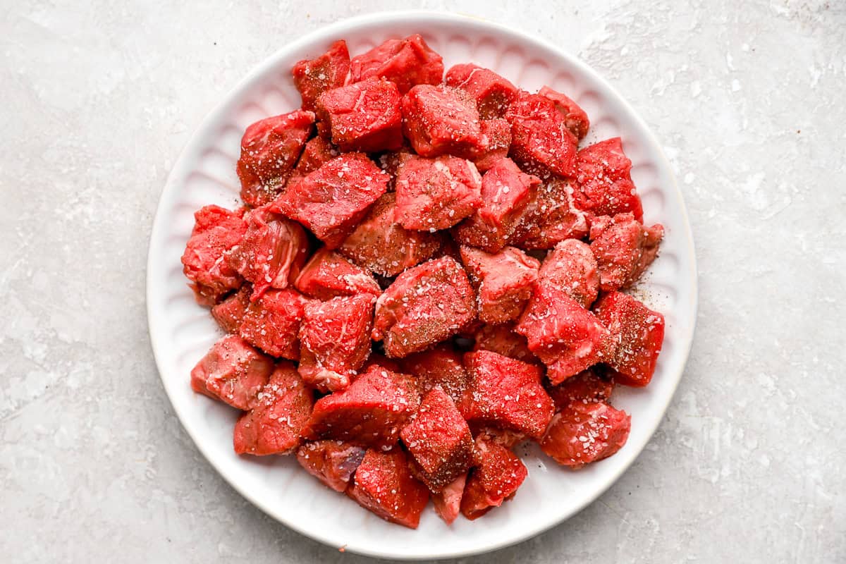 Cubed steak seasoned with salt and pepper on a plate for garlic butter steak bites.