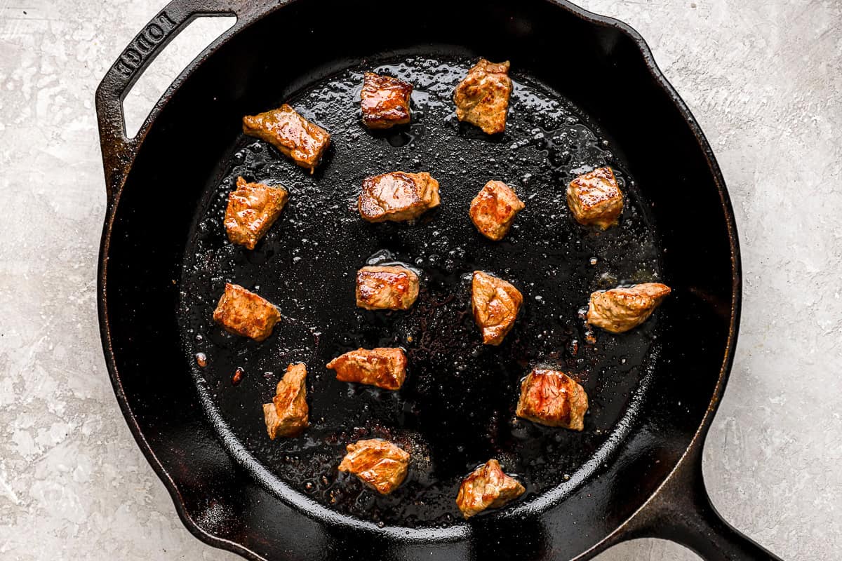 Steak bites searing in a cast iron skillet for garlic butter steak bites.