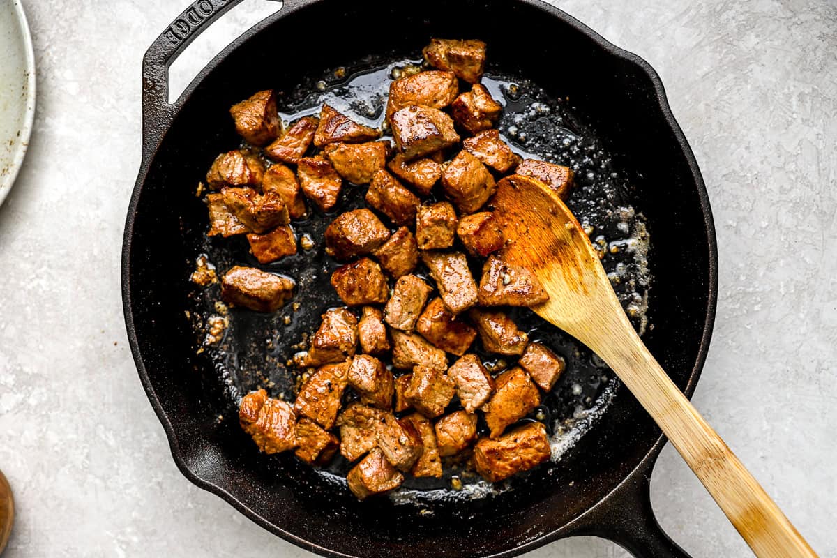 Steak bites tossed in garlic butter sauce in a cast iron skillet.