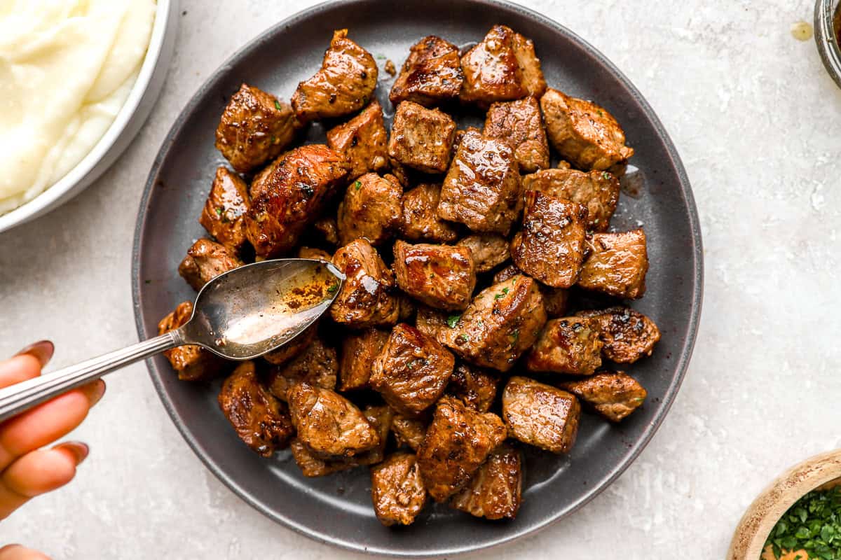 Garlic butter steak bites on a plate with melted butter being spooned over the top