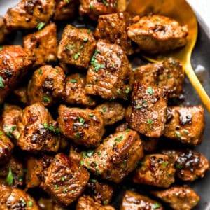 Garlic butter steak bites with browned edges and fresh parsley in a bowl.