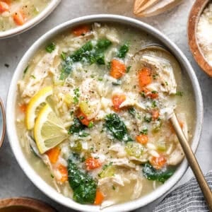 Lemon chicken orzo soup in a bowl topped with spinach, shredded chicken, carrots, and lemon slices