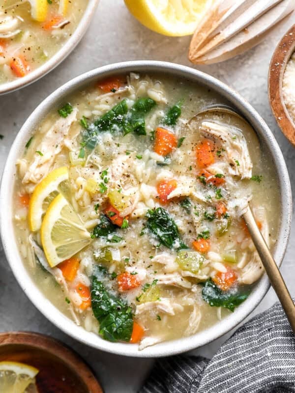 Lemon chicken orzo soup in a bowl topped with spinach, shredded chicken, carrots, and lemon slices