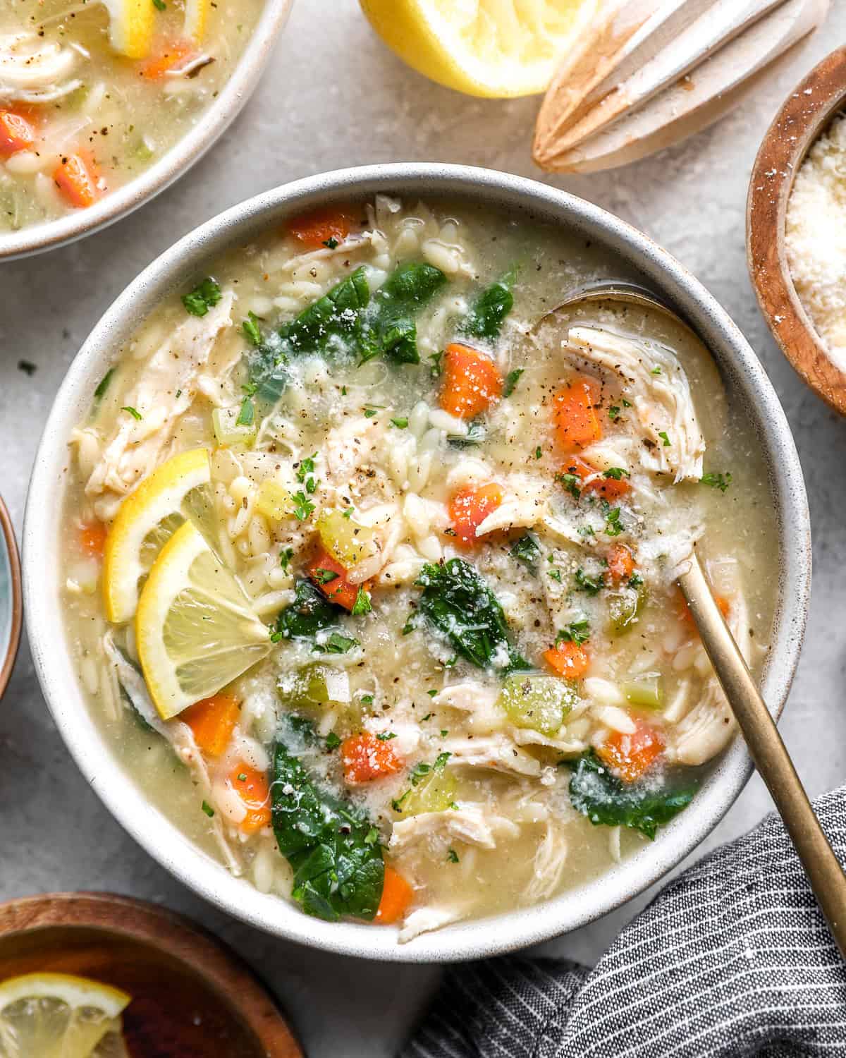Lemon chicken orzo soup in a bowl topped with spinach, shredded chicken, carrots, and lemon slices