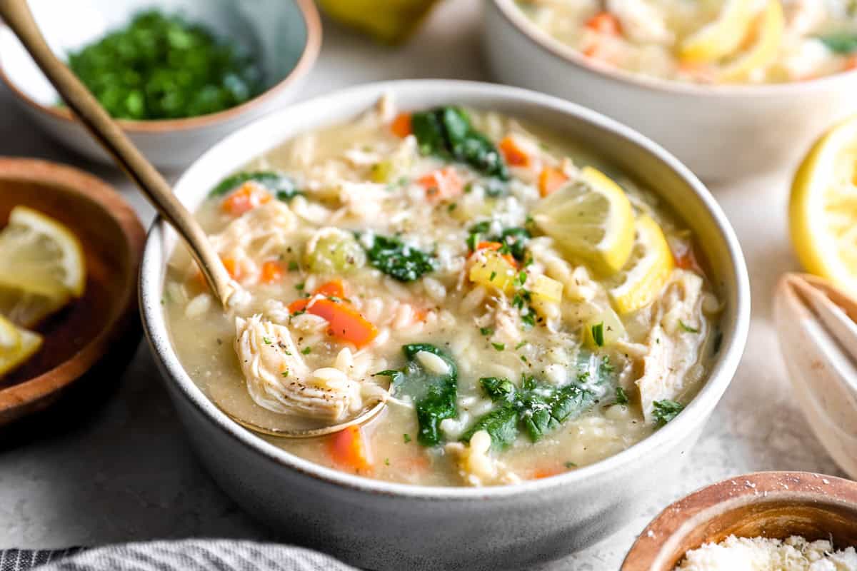 Bowl of lemon chicken orzo soup topped with parmesan, parsley, and lemon slices