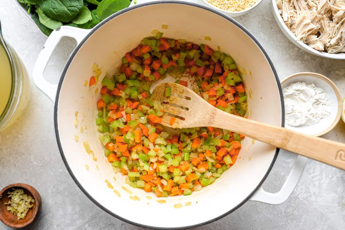 Diced onions, carrots, and celery sautéing in a large pot for lemon chicken orzo soup