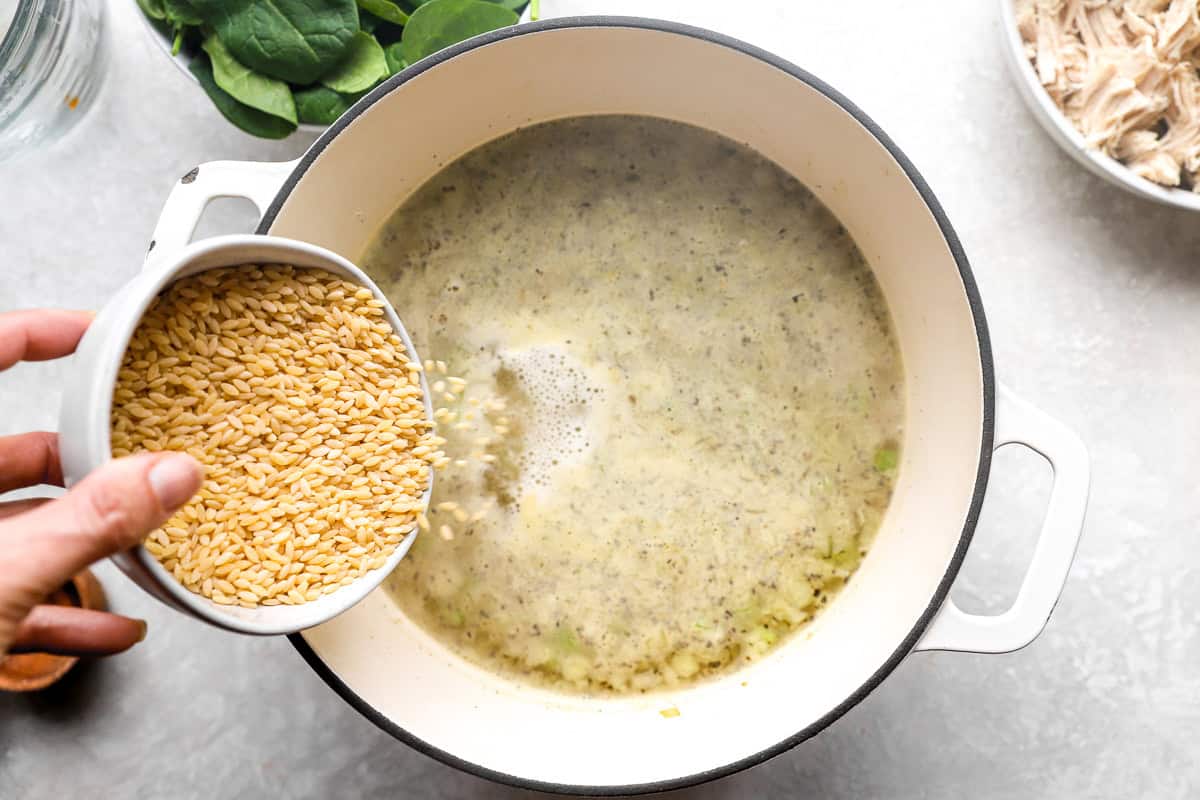 Orzo pasta being added to simmering broth in a pot for lemon chicken orzo soup