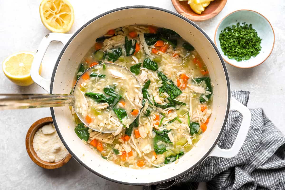 Spinach stirred into lemon chicken orzo soup with chicken, orzo, and vegetables in a pot