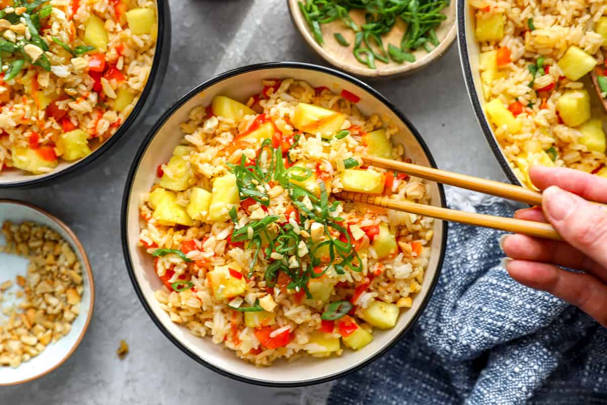 Serving of pineapple fried rice in a bowl with chopsticks picking up a bite