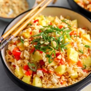 Bowl of pineapple fried rice topped with green onions, cashews, and sriracha with chopsticks on the side