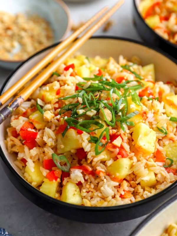 Bowl of pineapple fried rice topped with green onions, cashews, and sriracha with chopsticks on the side
