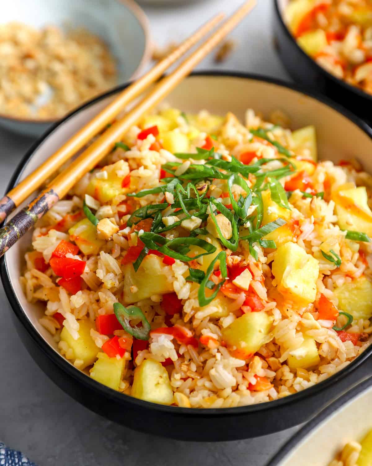 Bowl of pineapple fried rice topped with green onions, cashews, and sriracha with chopsticks on the side