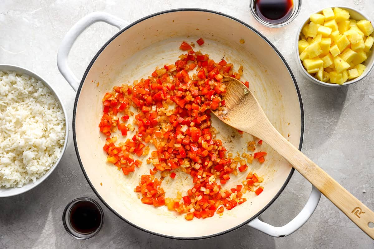Diced red bell pepper and onion cooking in a skillet with garlic and spices