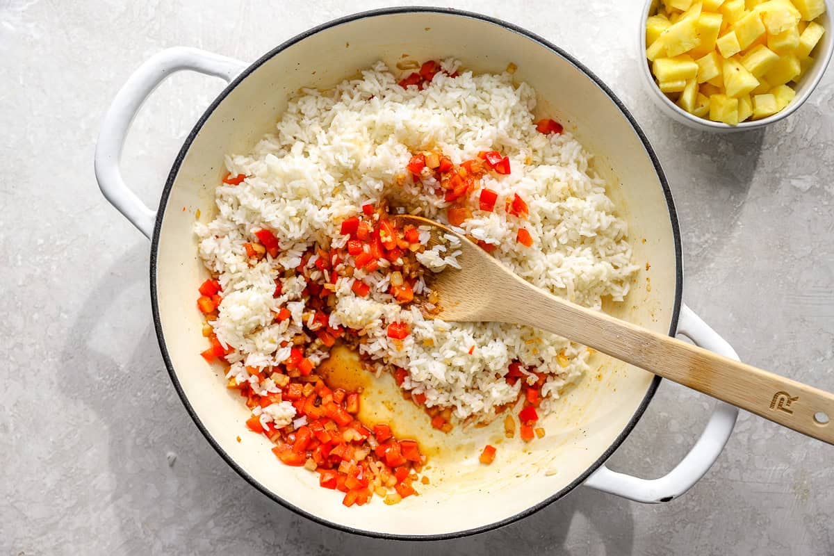 Cooked jasmine rice being added to sautéed vegetables in a skillet