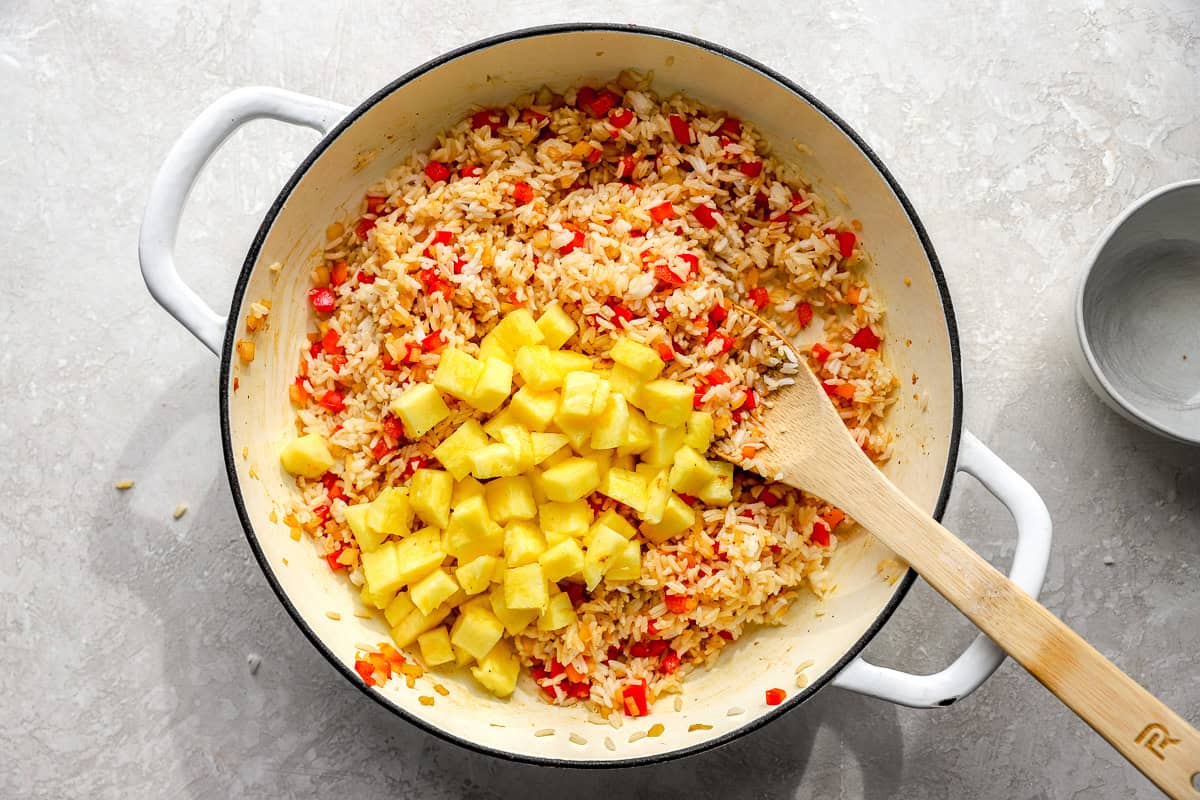 Fresh pineapple chunks added to fried rice in a skillet