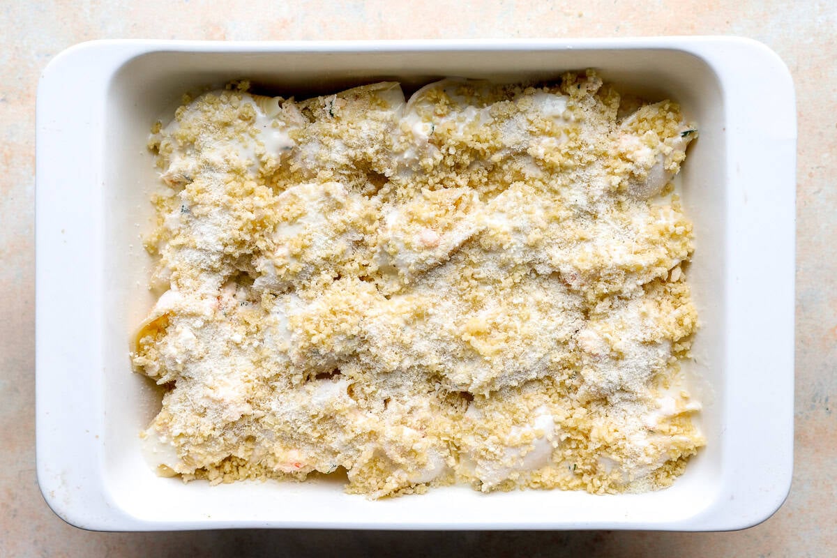 Seafood stuffed shells topped with breadcrumbs and parmesan in a casserole dish before baking.