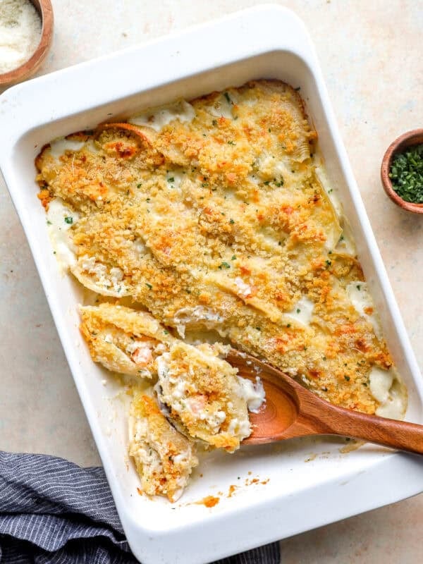 Baked seafood stuffed shells in a white casserole dish topped with golden breadcrumbs and parmesan, with a spoon scooping out a shell.