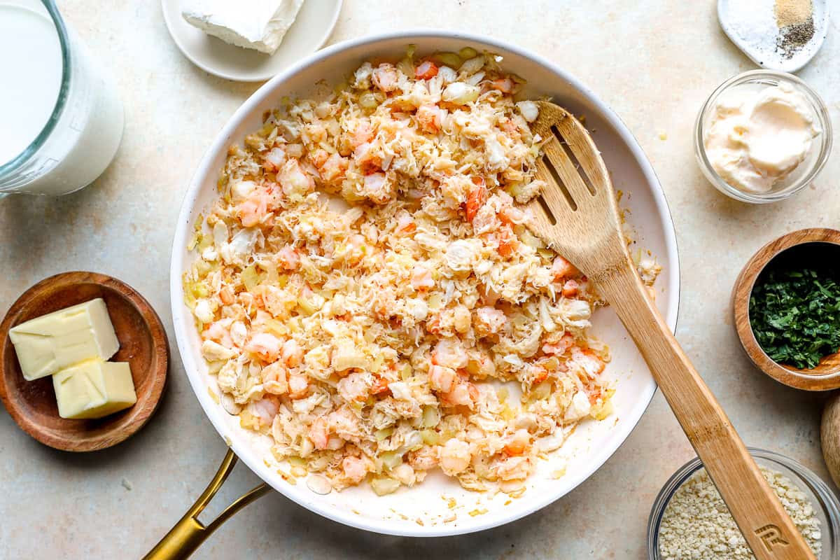 Shrimp and lump crab meat cooking with sautéed onions in a skillet for seafood stuffed shells.