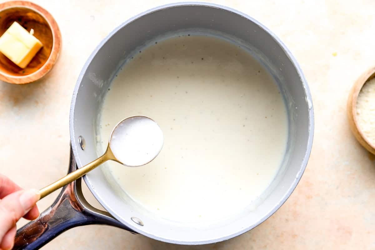 Homemade cream sauce for seafood stuffed shells simmering in a saucepan until thickened.