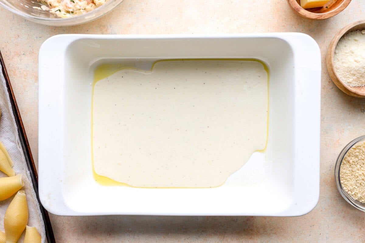 Cream sauce spread in the bottom of a baking dish for assembling seafood stuffed shells.