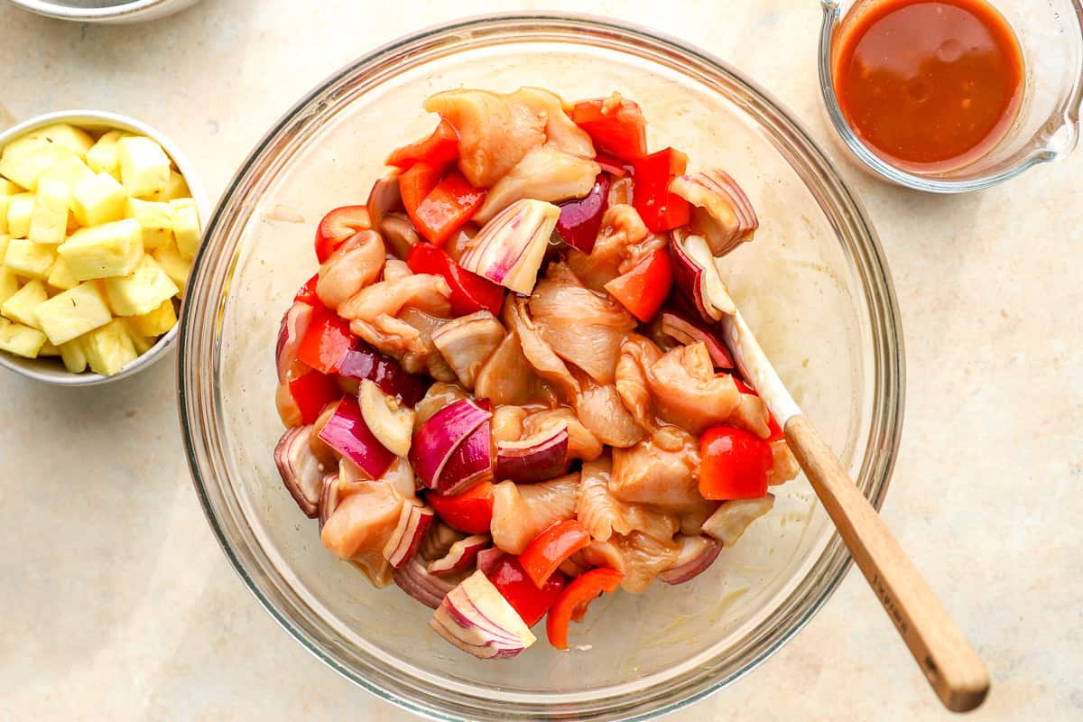 Raw chicken, red onion, and bell peppers tossed in Hawaiian sauce in a mixing bowl