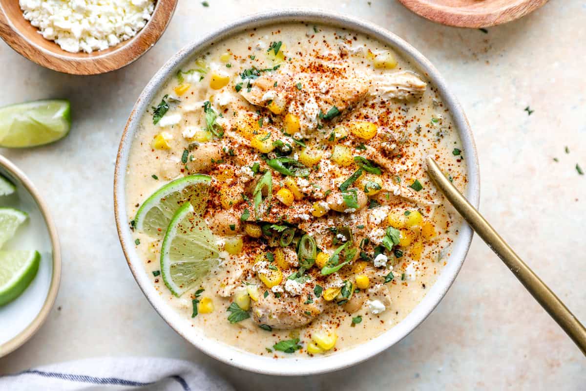Street corn white chicken chili topped with cotija cheese, cilantro, corn, chili powder, and lime in a serving bowl