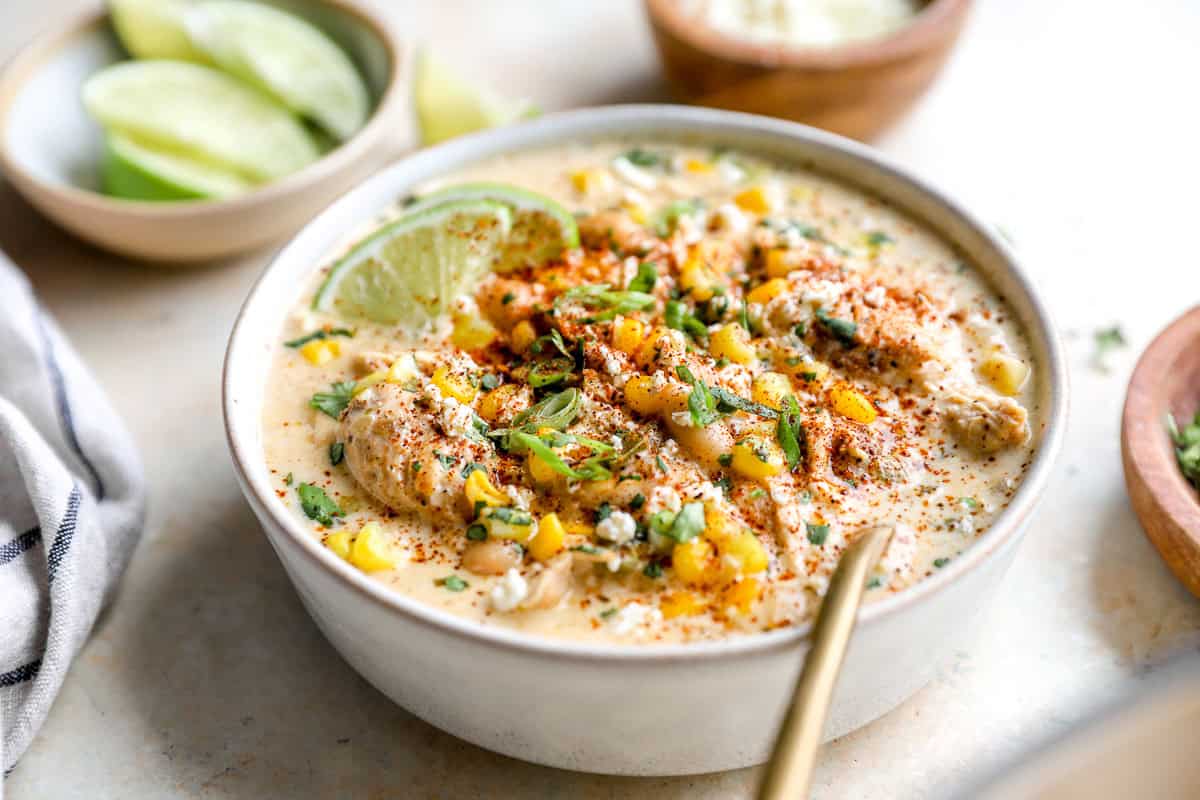 Close-up of creamy white chicken chili with corn, shredded chicken, cotija cheese, and fresh herbs in a bowl