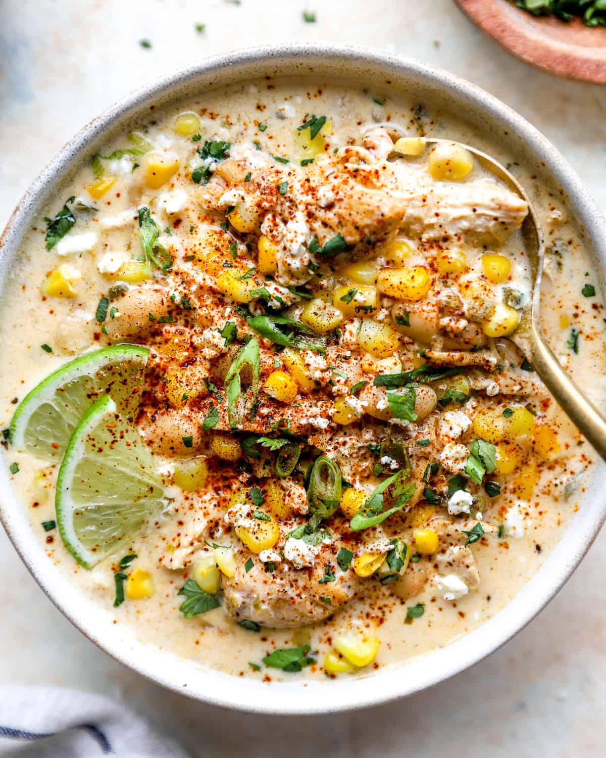 Street corn white chicken chili topped with cotija cheese, corn, cilantro, chili powder, and lime in a bowl
