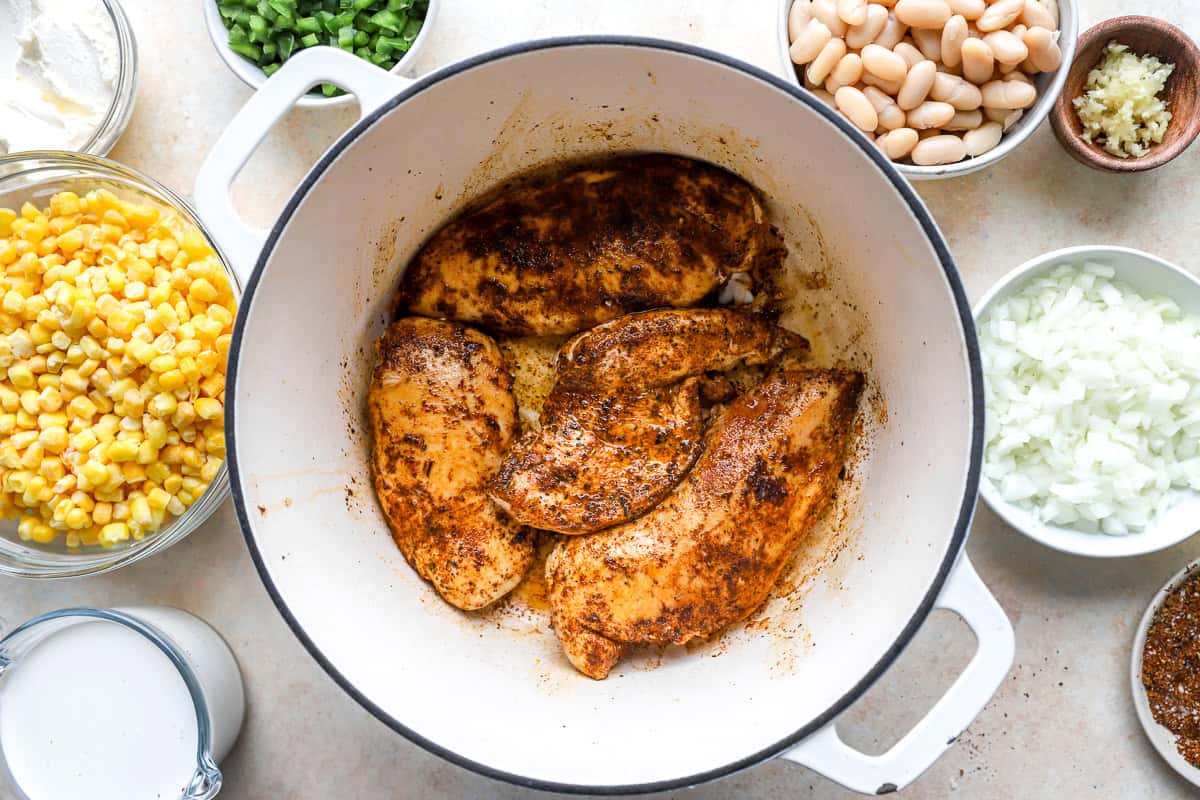Chicken breasts searing in a Dutch oven with spices until lightly browned for white chicken chili